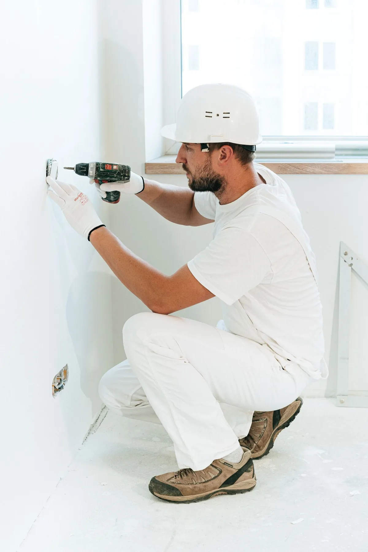 Eletricista com equipamentos de proteção instalando uma tomada em um apartamento